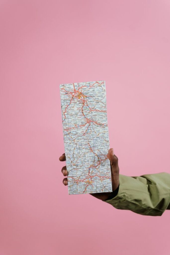 Close-up of a hand holding a folded paper map against a pastel pink background.