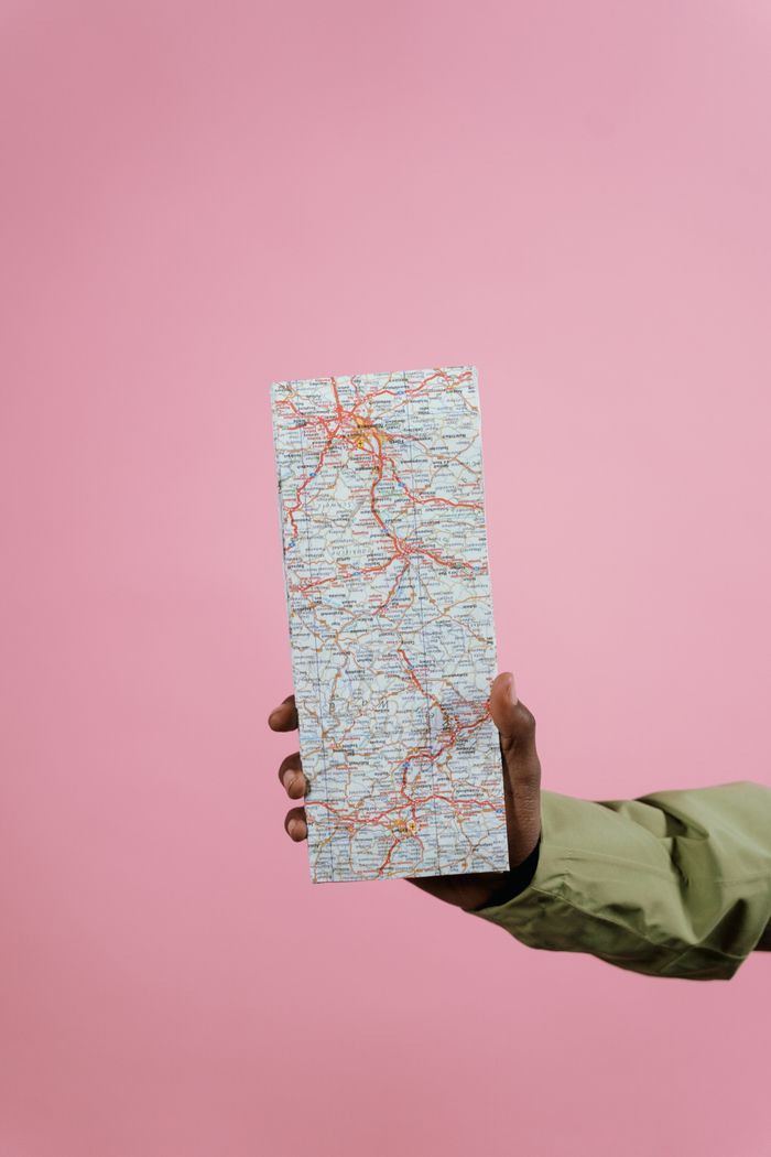 Close-up of a hand holding a folded paper map against a pastel pink background.